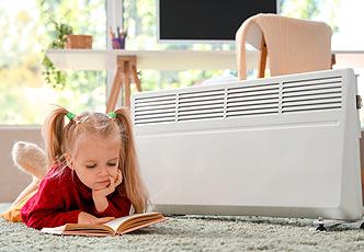 niña leyendo junto a un radiador eléctrico