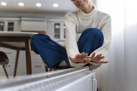 mujer calentándose las manos con el radiador eléctrico